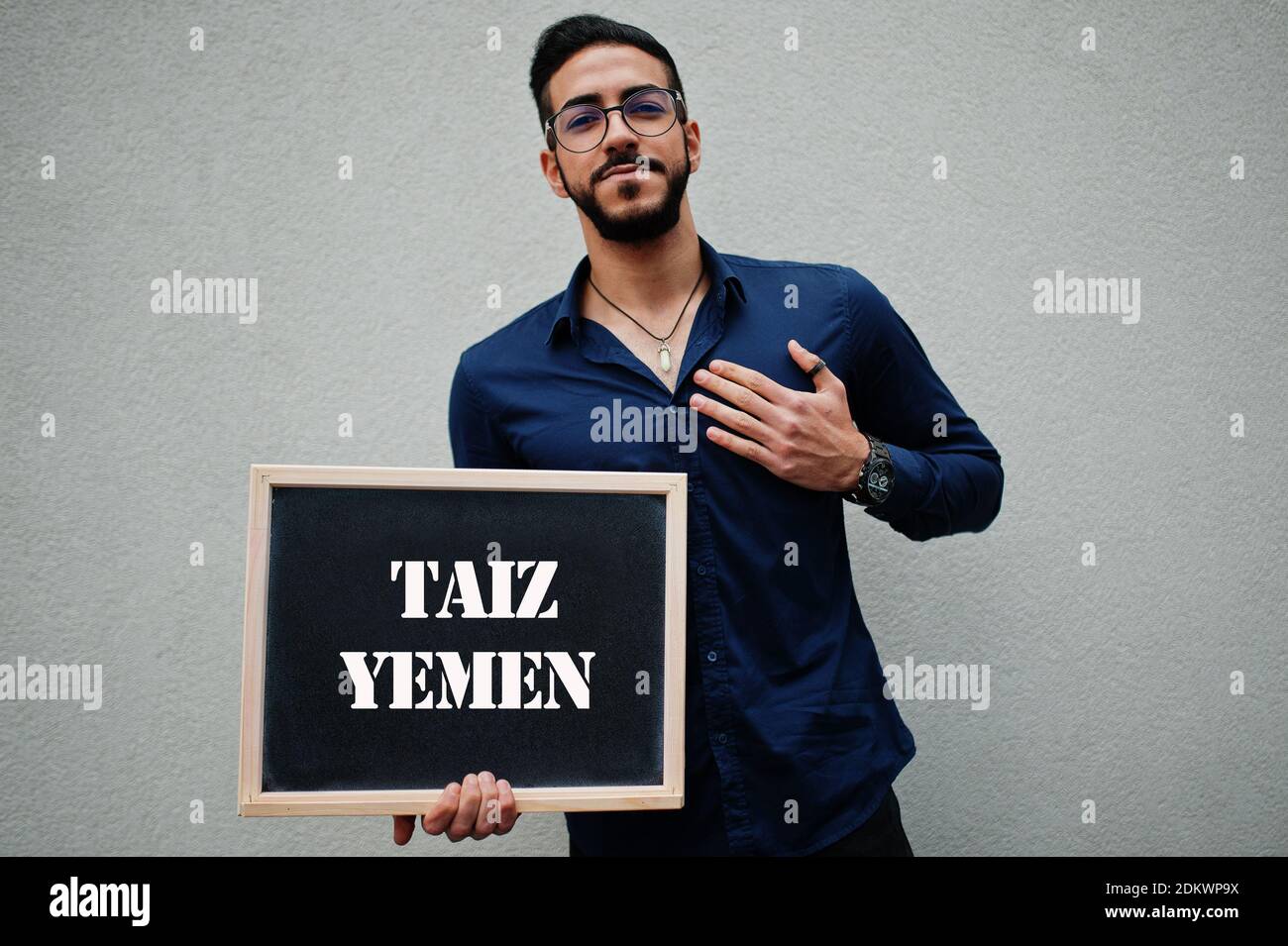 Araber tragen blaues Hemd und Brillen halten Brett mit Taiz Jemen Inschrift. Größte Städte in der islamischen Welt Konzept. Stockfoto