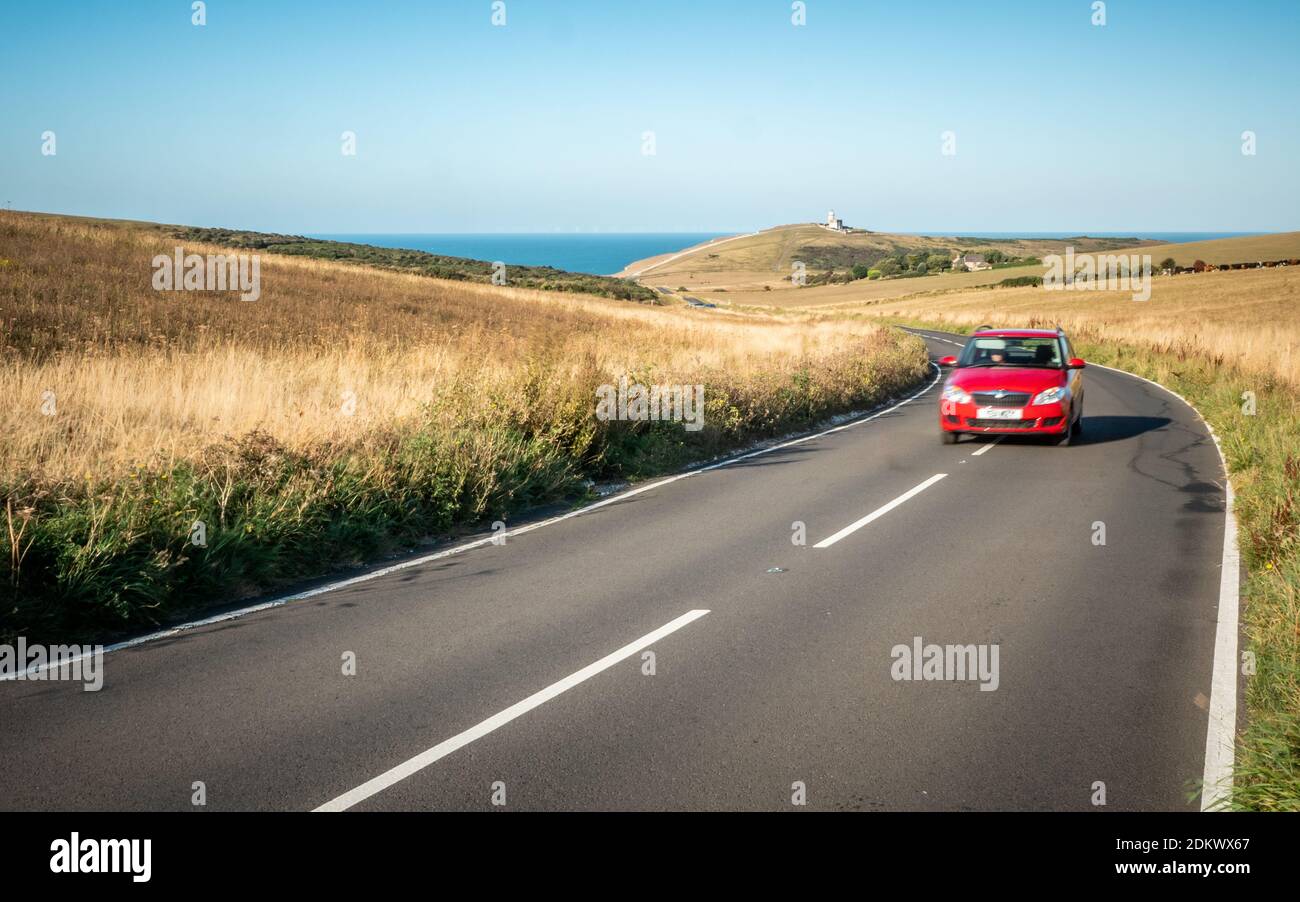 Roadtrip; South Downs, England. Ein Auto auf einer kurvenreichen Straße in East Sussex mit dem Leuchtturm Belle Tout und dem Ärmelkanal in der Ferne. Stockfoto