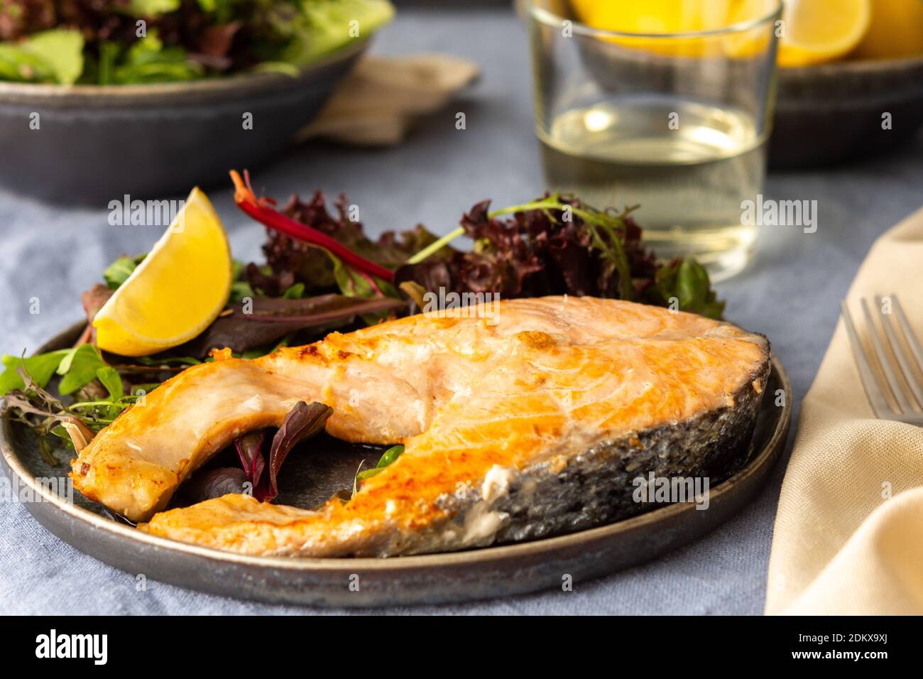 Gebratenes Lachssteak mit Salat auf einem Teller, Weißwein im Glas, leckeres herzhaftes Abendessen oder Mittagessen Stockfoto