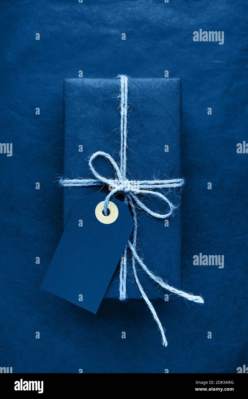 Blaues Geschenk mit blauem Geschenkanhänger auf blauem Hintergrund. Farbe des Jahres 2020 klassisch blau getönt. Urlaubskonzept. Draufsicht Stockfoto