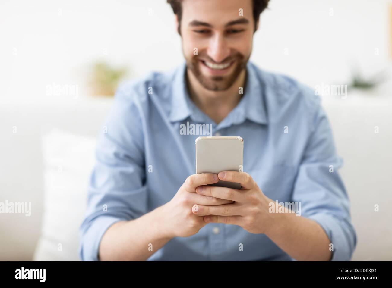 Happy Guy Mit Smartphone Texting Sitzen Auf Der Couch Zu Hause Stockfoto