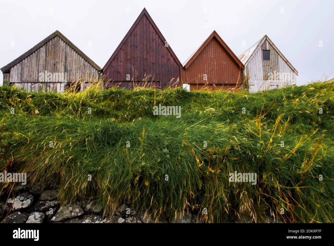 Scharf dreieckige Spitzdächer von Metallgaragen/Lagerhäusern in Form von Zickzack, gelegen auf einem grasbewachsenen Hügel entlang eines Ufers. Färöer-Inseln Stockfoto