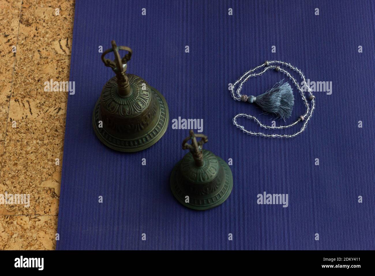 Metallglocken auf Yogamatte mit mala-Kette an der Seite. Draufsicht auf Zubehör für Meditationsritual. Entspannen, Zen-Konzepte Stockfoto