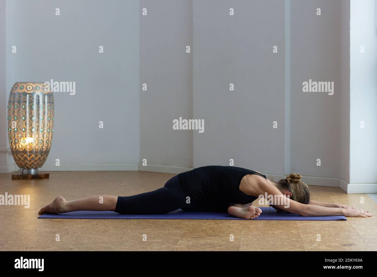 Flexible Frau, die sich im Yoga-Studio auf Taubenpose legt. Weibliche Yogi auf schwarzem Outfit führt schlafenden Schwan mit einem Bein gestreckt und die Arme nach vorne Stockfoto