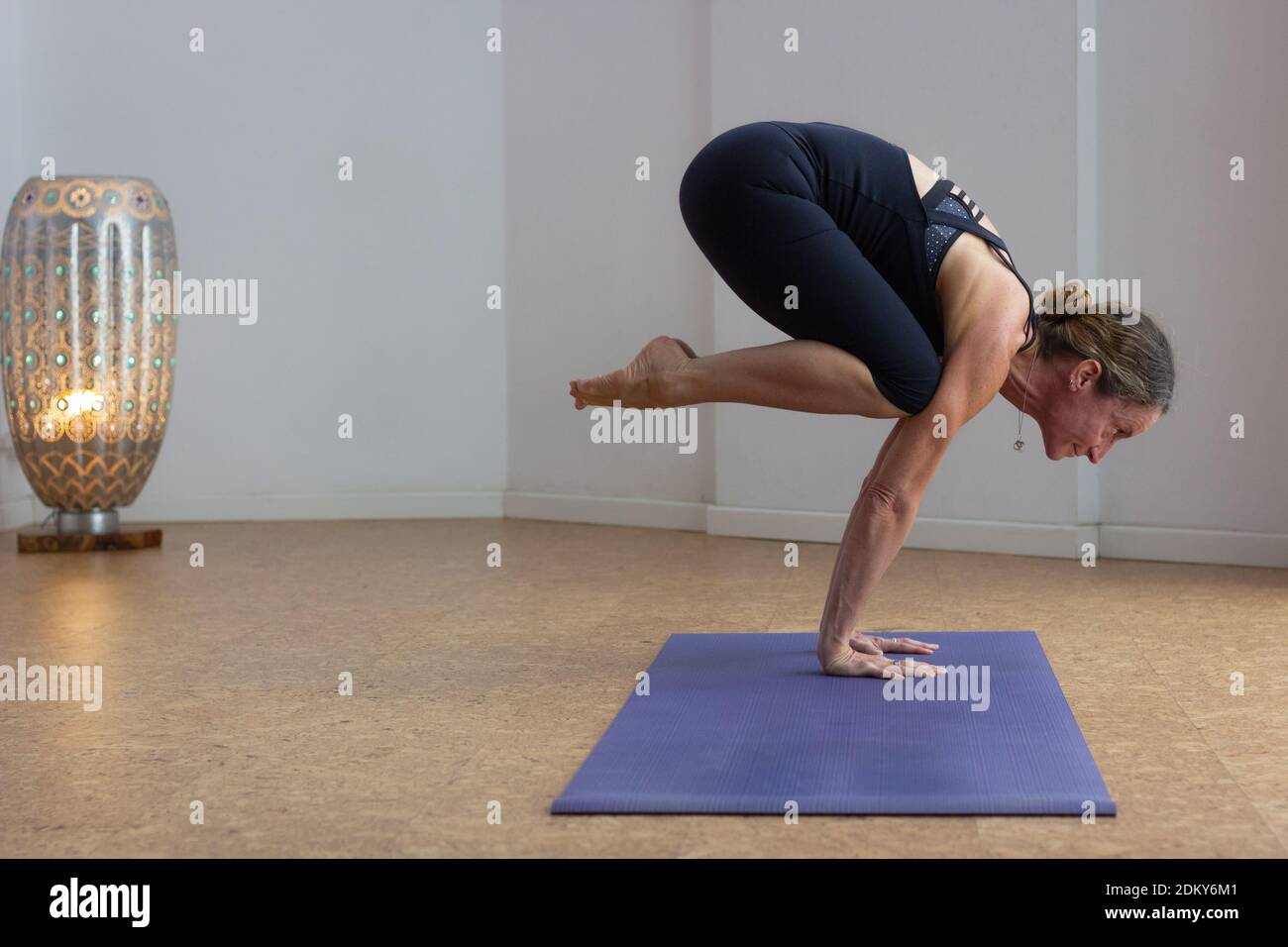 Starke Frau in bakasana Yoga-Pose stehen auf Händen mit gefalteten Beinen allein im Studio. Flexible weibliche Yogi üben ashtanga Zwischenserie Stockfoto