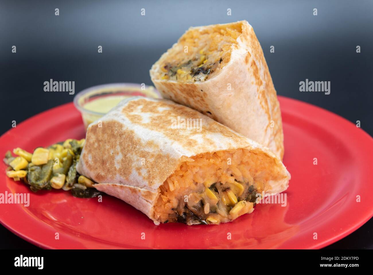 Gemüse Burrito mit frischem Gemüse in zwei Hälften geschnitten geladen und präsentiert auf einem roten Teller. Stockfoto