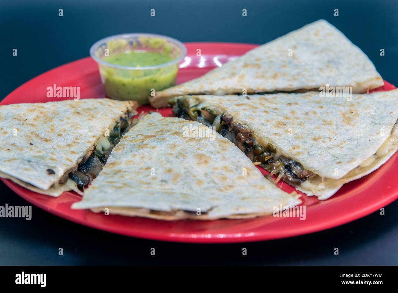 Veggie quesadilla beladen mit frischem Gemüse, geschmolzenem Käse und Mehl Tortilla und präsentiert auf einem roten Teller. Stockfoto