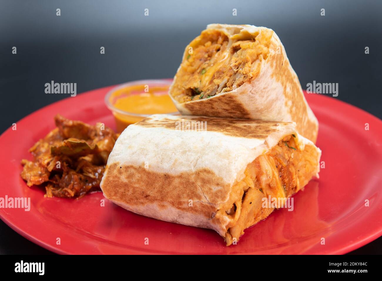 Huhn Burrito mit frischem Fleisch in zwei Hälften geschnitten geladen und präsentiert auf einem roten Teller. Stockfoto