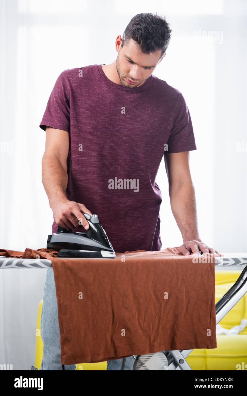 Junger Mann bügelt T-Shirt auf dem Boot zu Hause Stockfoto