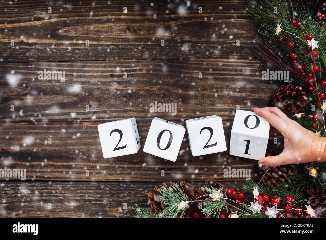 Frau Hand kippt Neujahr 2020 Holz Kalender Blöcke zu 2021. Weihnachtsbaumlichter, Kiefernzweige, rote Winterbeeren und Schnee. Draufsicht. Stockfoto