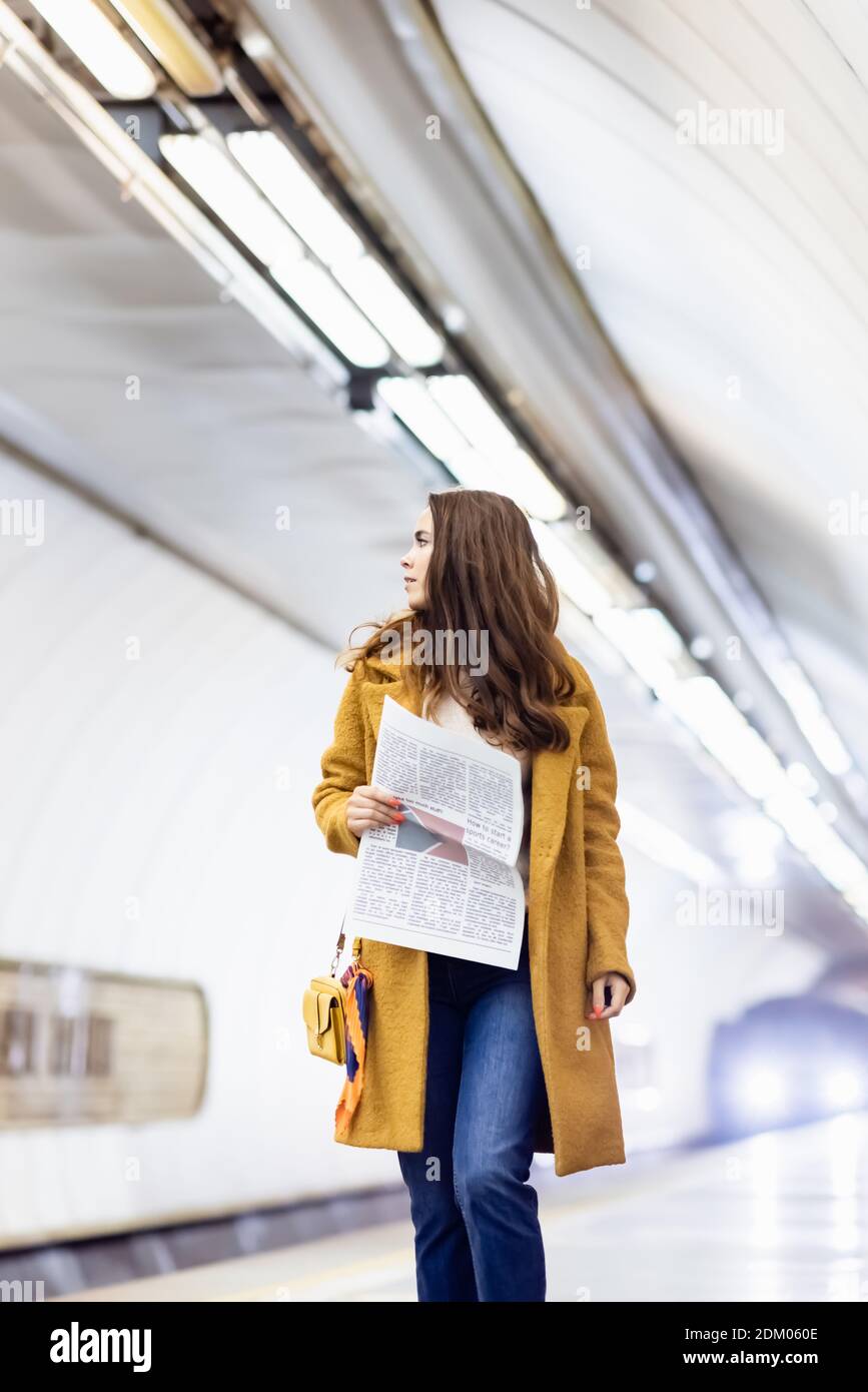 Junge Frau im Mantel mit Zeitung beim Spaziergang entlang der U-Bahn Plattform Stockfoto