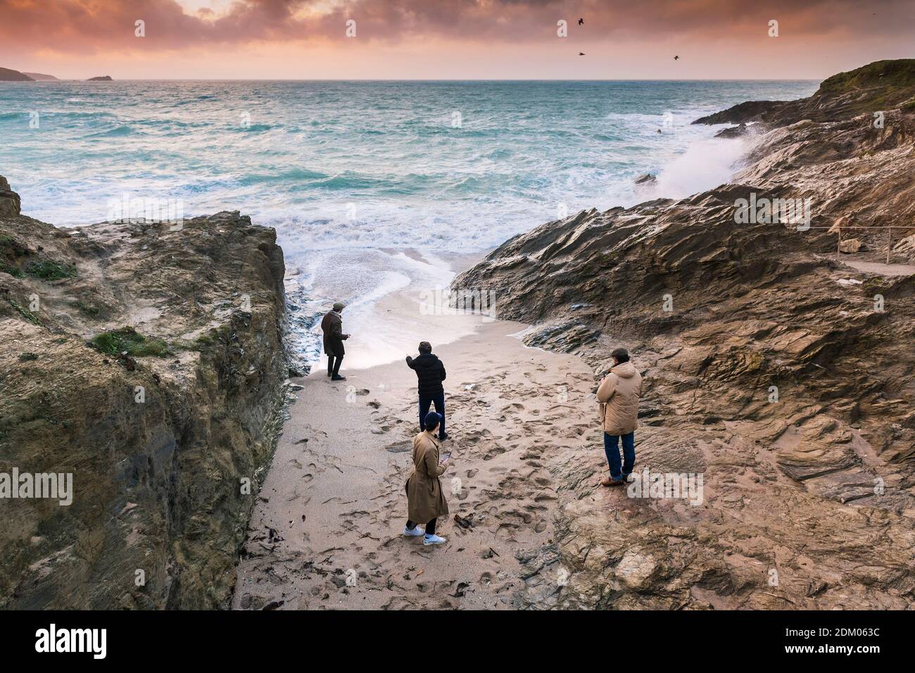 Abendlicht, als vier junge Männer am Strand in einer kleinen Bucht bei Little Fistral in Newquay in Cornwall stehen. Stockfoto