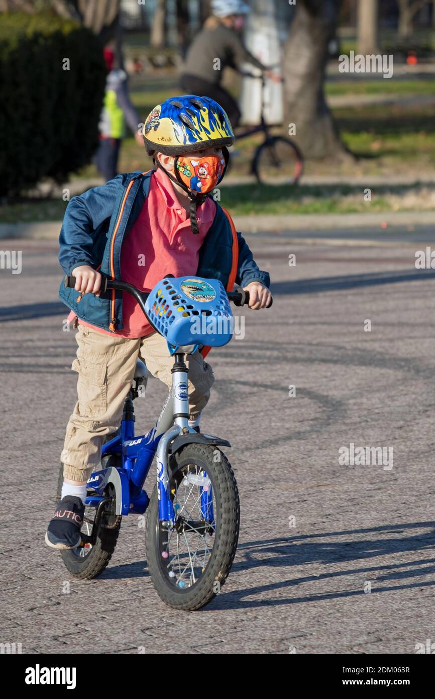 Ein farbenfrohes Foto eines Pre-Teen, der mit Helm und Maske auf seinem Fahrrad unterwegs ist. In Flushing Meadows Corona Park in Queens, New York. Stockfoto