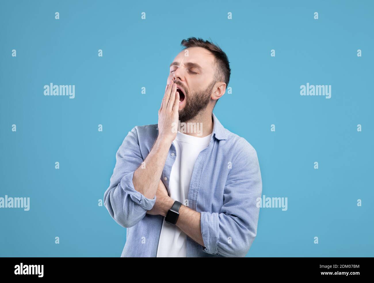 Gelangweilter junger Kerl, der offenen Mund mit der Hand über blauem Studiohintergrund bedeckt Stockfoto