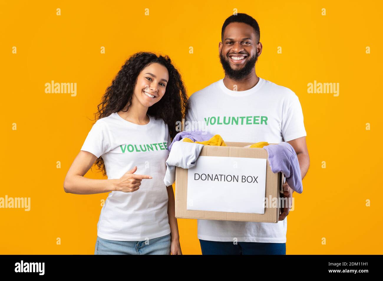 Zwei Fröhliche Freiwillige Halten Spende Box Auf Gelbe Studio Hintergrund Stockfoto