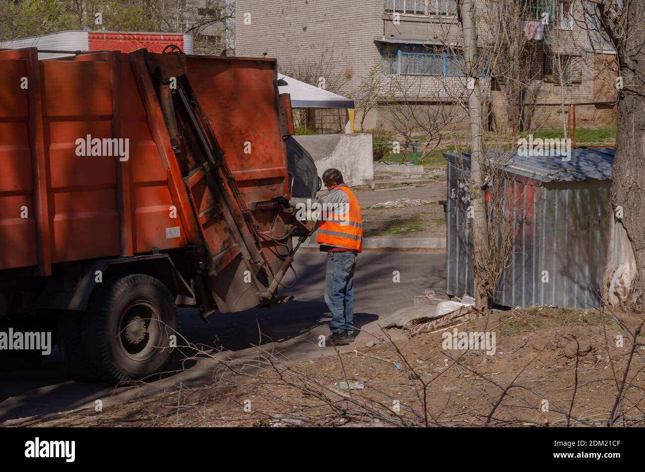 Nikolaev, Ukraine - 1. April 2020: Ein Mann in einer orangefarbenen Weste bedient die Hebel auf einem Müllwagen. Stockfoto