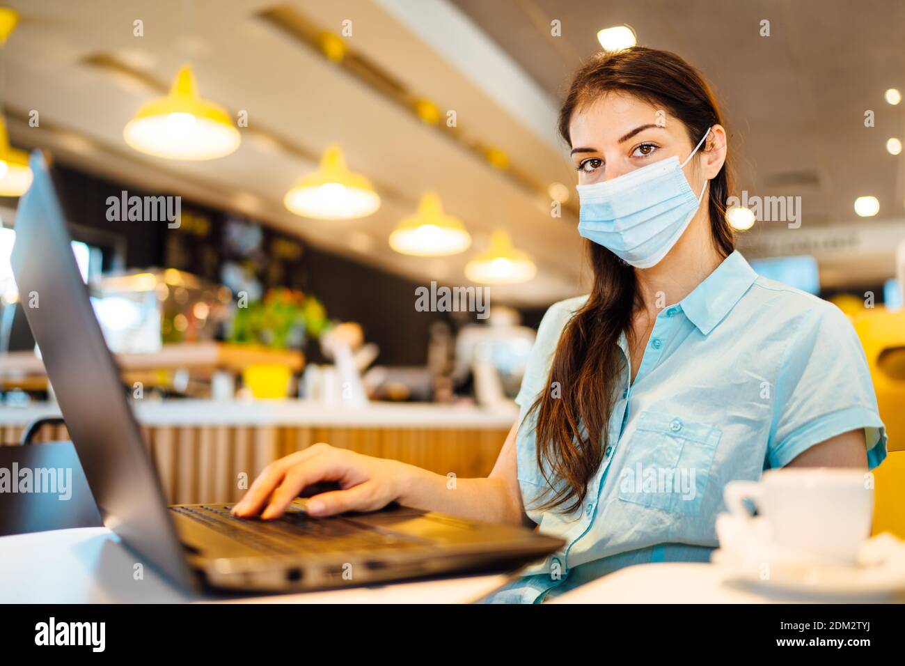 Junge Frau in einem öffentlichen Ort, die auf Laptop, Tragen von Schutzmaske indoor.Online-Ausbildung Ausbildung und freiberufliche Arbeit.Studieren Remote.O Stockfoto