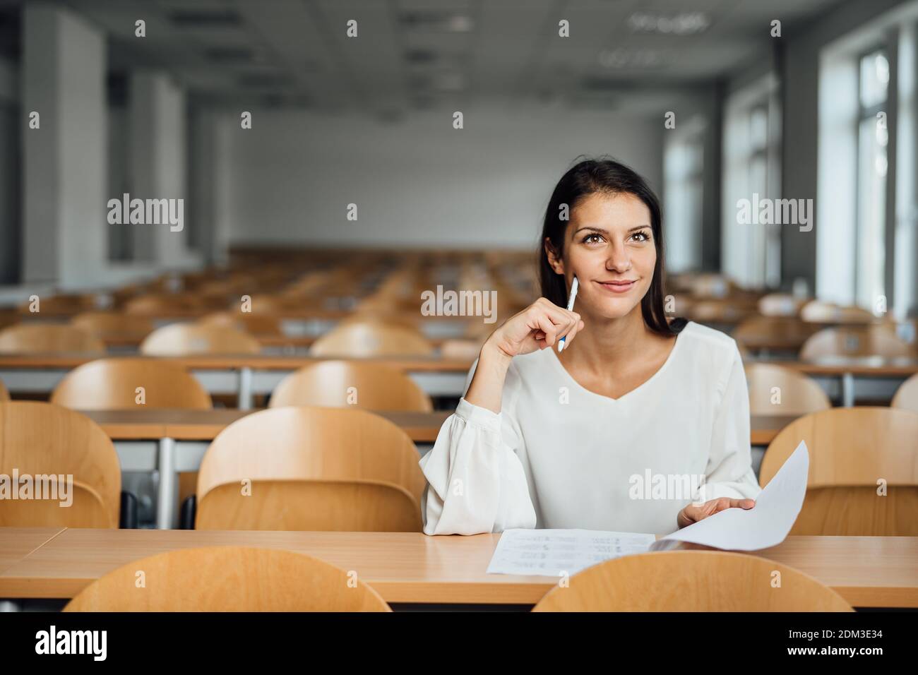 Kenntnisreiche Schülerin, die eine einfache Prüfung in einem leeren Amphitheater abgelegt hat. Ein optimistischer Student, der einen Test in der Klasse abgibt. Glückliche Frau mit Stress fre Stockfoto