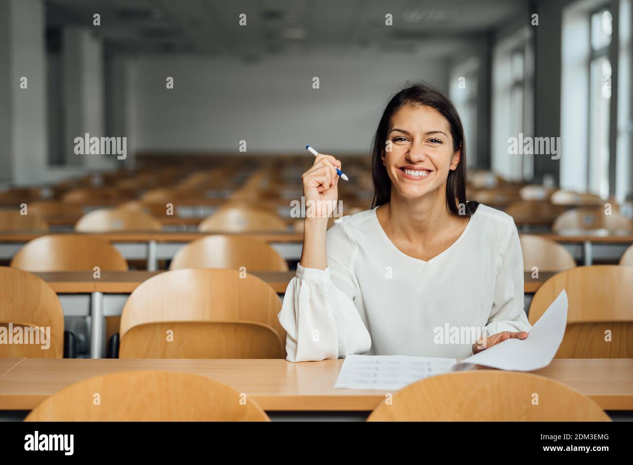 Kenntnisreich lächelnder Student, der eine einfache Prüfung in einem leeren Amphitheater abnimmt. Ein optimistischer Student, der einen Test in der Klasse abgibt. Glückliche Frau mit Stress Fr. Stockfoto
