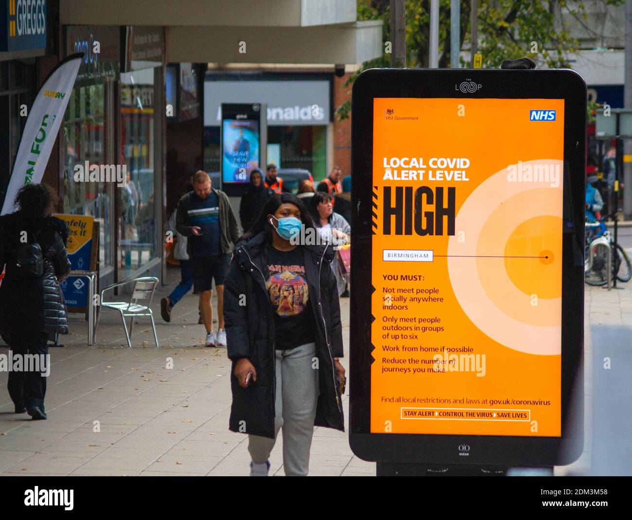 Lokale Warnstufe hohe Schilder rund um das Stadtzentrum von Birmingham auf der Bull Street in der Nähe des Bullring Shopping Centre. Fußgänger passieren das Werbebanner in der zweiten Sperrstufe. Stockfoto