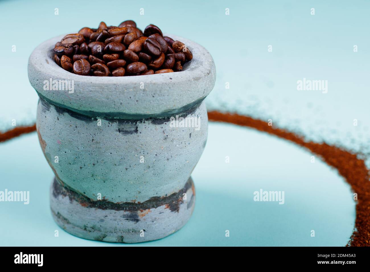 Geröstetes Vollkaffeekorn auf einem mexikanischen Steinmörtel, umgeben von einem Kreis aus gemahlenem Kaffee, und einem hellblauen Hintergrund Stockfoto