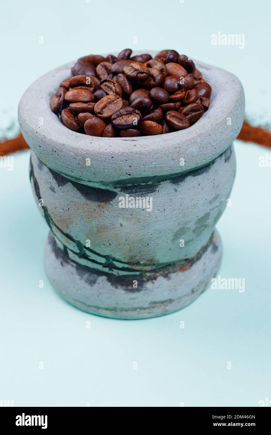 Geröstetes Vollkaffeekorn auf einem mexikanischen Steinmörtel, umgeben von einem Kreis aus gemahlenem Kaffee, und einem hellblauen Hintergrund Stockfoto