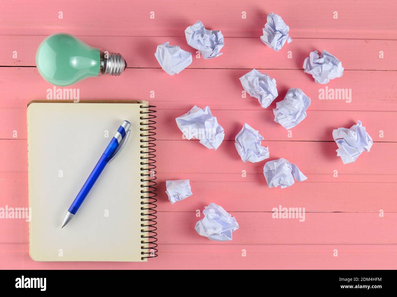 Notepad with a pen, incandescent bulb and crumpled white paper balls on a pink wooden table. Ideological concept, top view Stockfoto