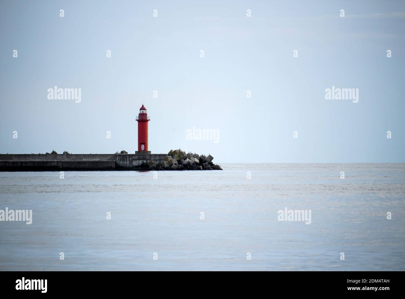 Ein roter Leuchtturm auf einem Wellenbrecher zwischen dem ruhigen Himmel Und das Meer Stockfoto