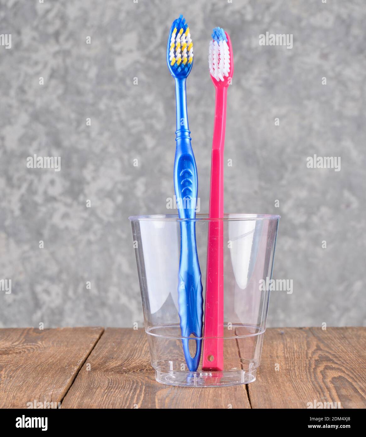 Zwei Zahnbürsten in einem transparenten Plastikbecher im Badezimmer Auf einem konkreten Hintergrund Stockfoto