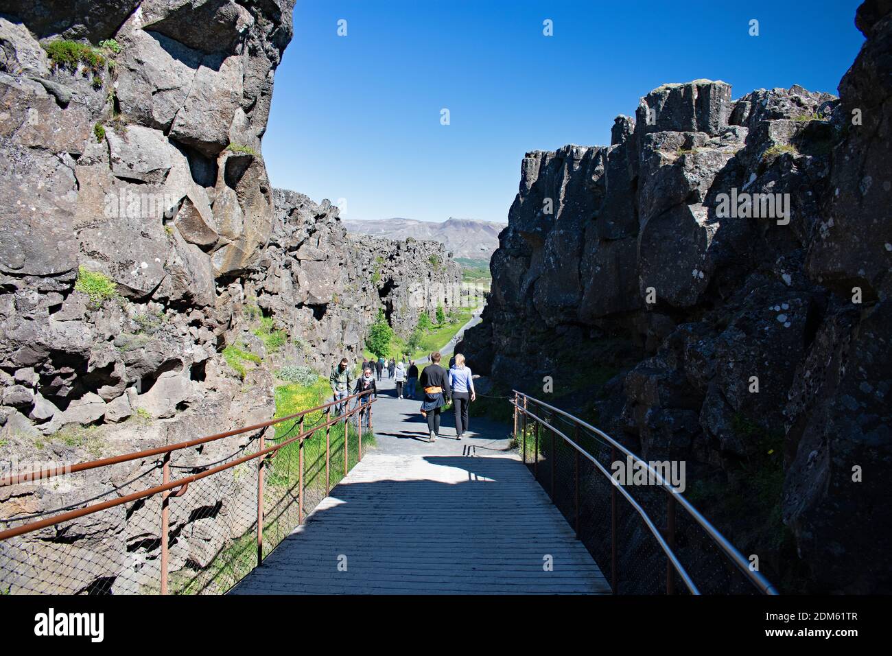 Besucher wandern entlang einer Promenade zwischen Haltepunkten in den Felsen, die durch die kontinentale Verschiebung, Thingvellir National Park erstellt wurden. Felsklippen säumen den Weg. Stockfoto