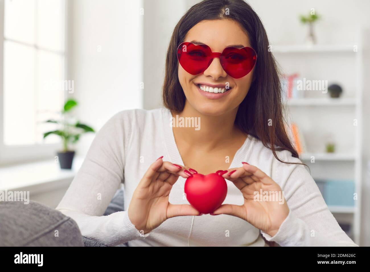 Dankbare Frau, die ein rotes Herz vor der Kamera hält, um ihrem Publikum Dankbarkeit auszudrücken. Stockfoto