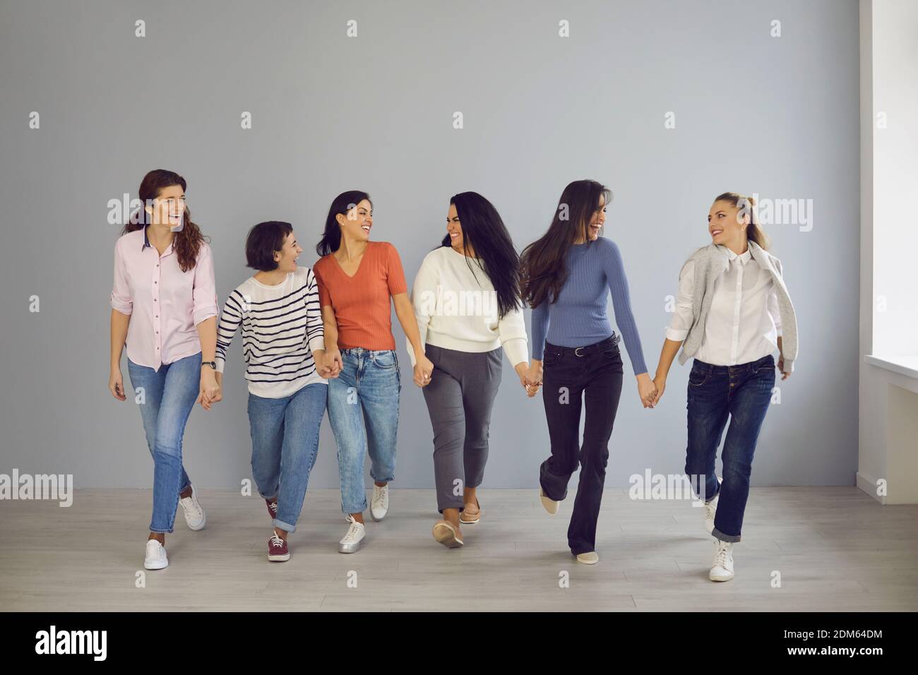 Gruppe von glücklichen, selbstbewussten Frauen, die Hand in Hand gehen und gegenseitige Unterstützung und Solidarität demonstrieren Stockfoto