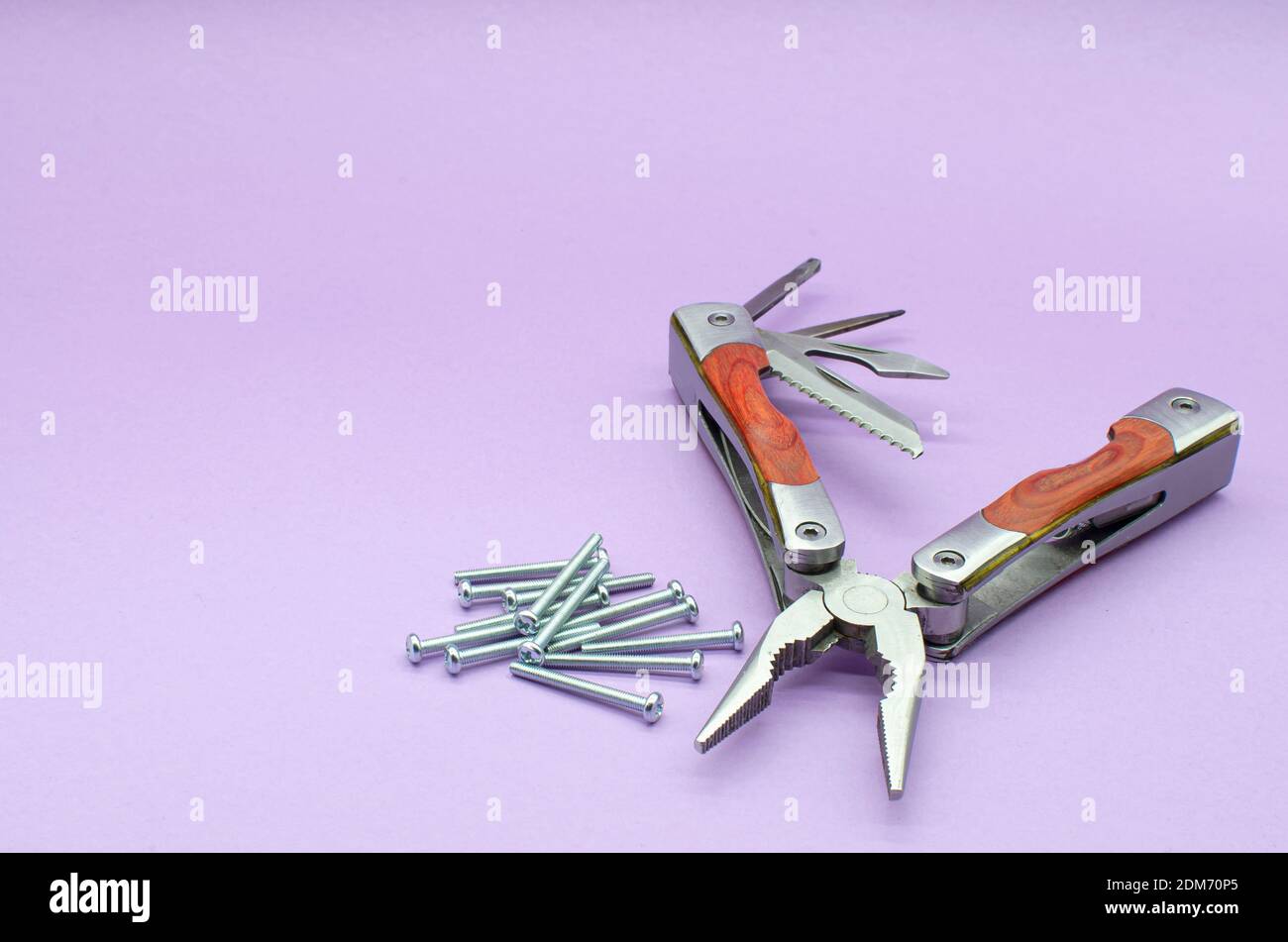 Holz-Multitool in Zange, Messer, Schraubendreher auf violettem Hintergrund, Schrauben. Reparatur. Fix Stockfoto