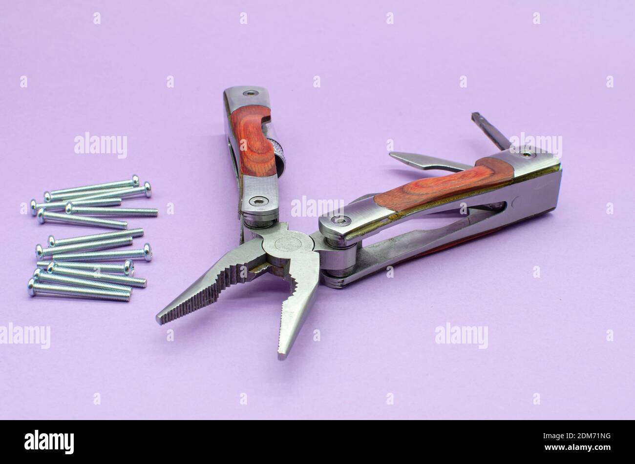 Holz-Multitool in Zange, Messer, Schraubendreher auf violettem Hintergrund, Schrauben. Reparatur. Fix Stockfoto