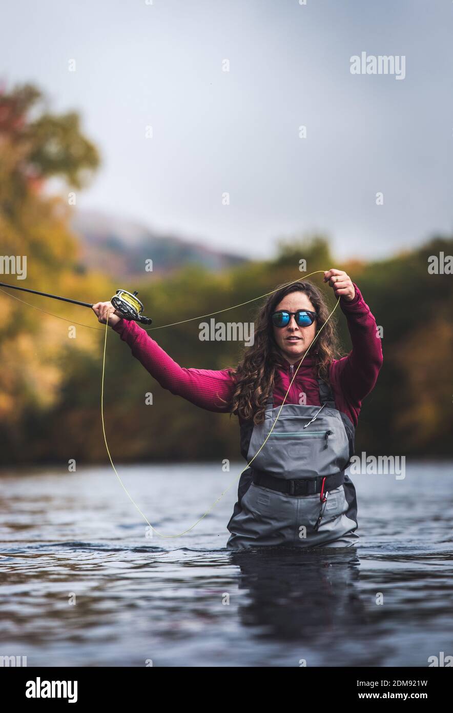 Frau in Watvögeln, die im Fluss mit herbstlichen Blättern hinter sich werfen Sie Stockfoto