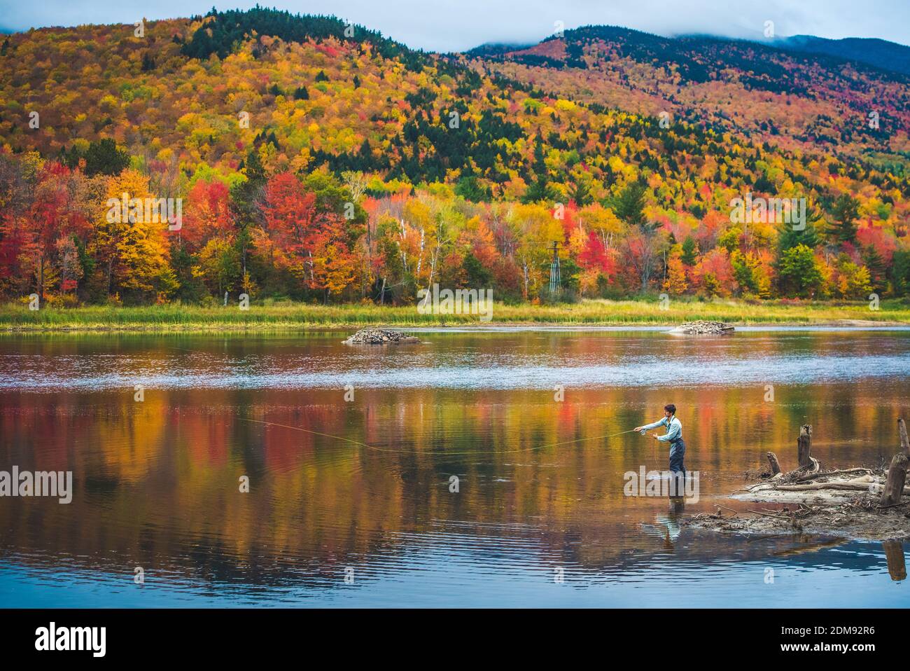 Fliegenfischer Gießen in Fluss mit hellen Laub und Berge Stockfoto