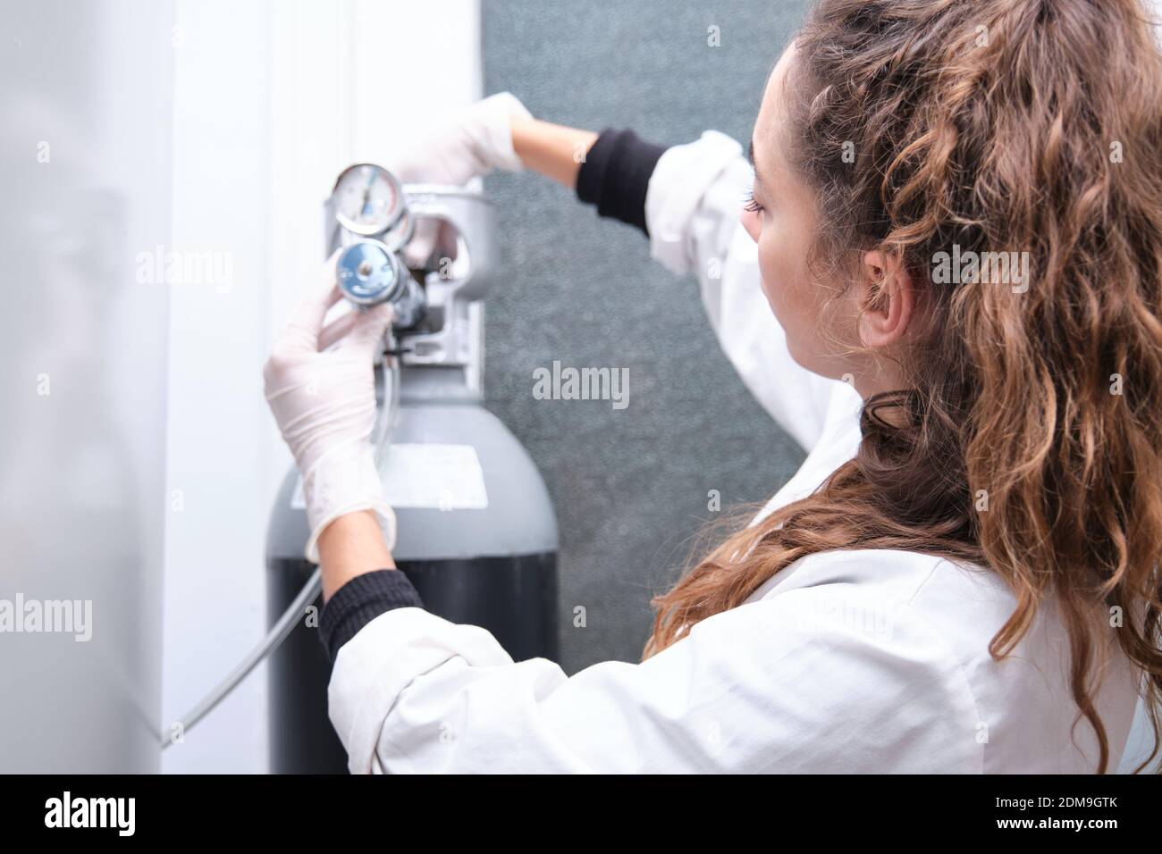 Junge Wissenschaftlerin beim Öffnen einer Gasflasche mit Manometer in einem spezialisierten Labor. Laborforschungskonzept. Stockfoto