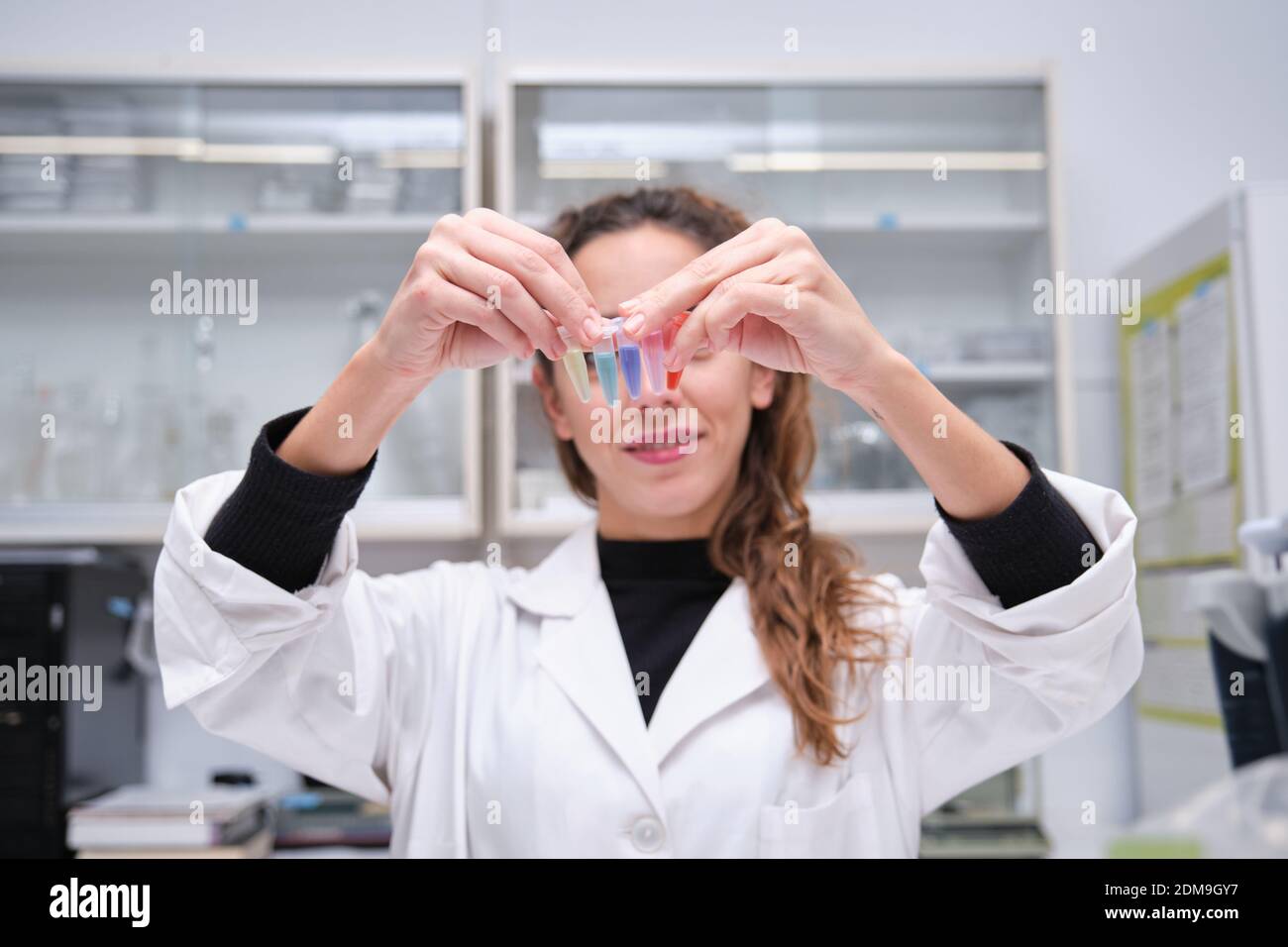 Junge Wissenschaftlerin lächelt mit eppendorfer Tuben vor ihrem Gesicht. Laborforschungskonzept. Stockfoto