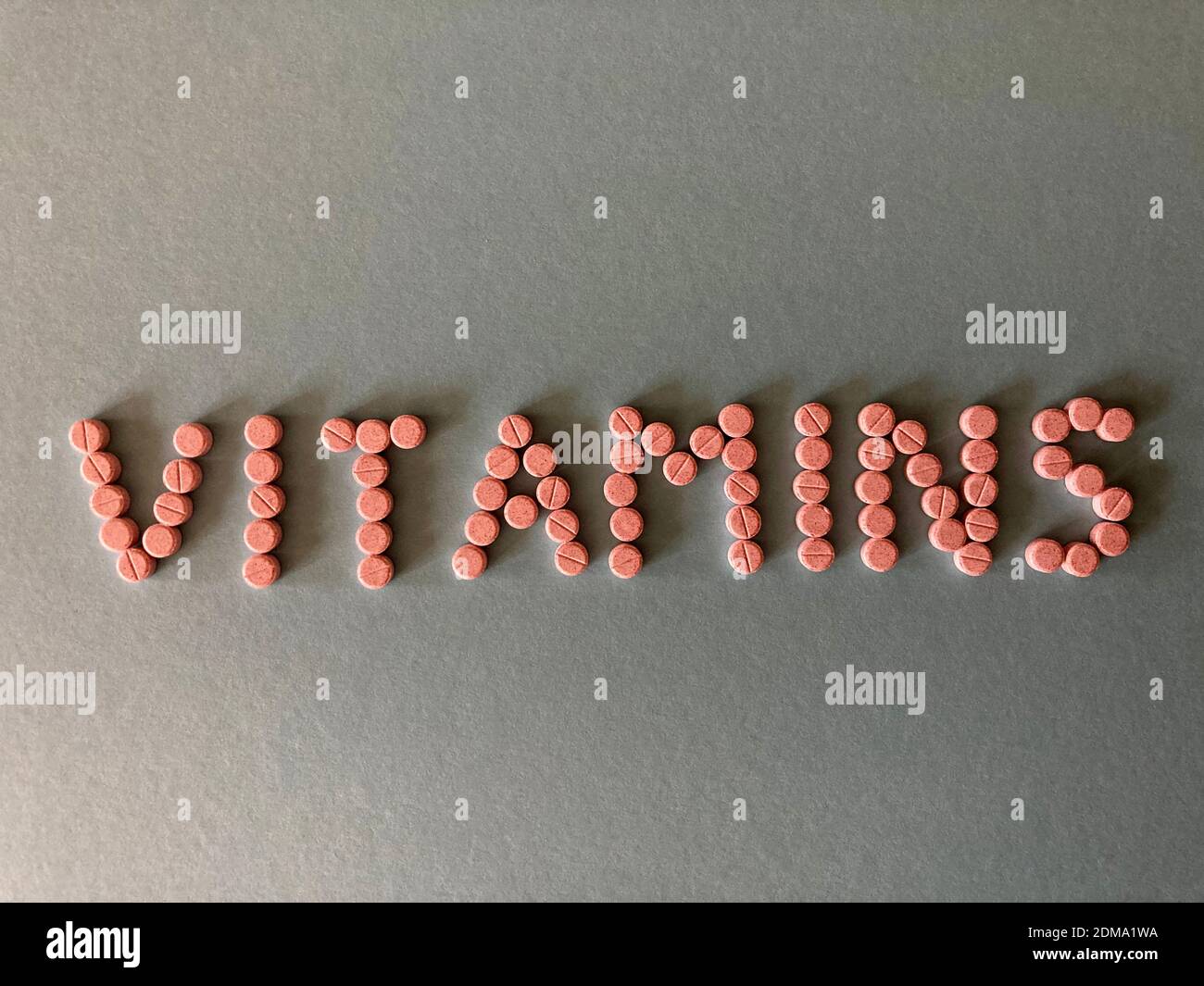Vitamine, Wort in kleinen rosa Tabletten, isoliert auf einfachem Hintergrund Stockfoto