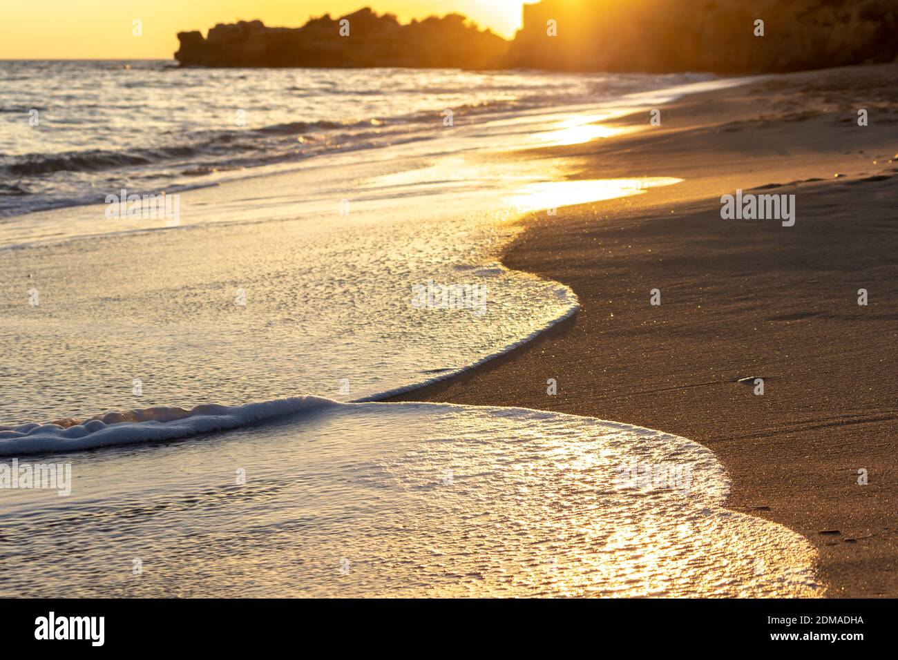 Sonnenuntergangsperspektive von der Strandküste mit goldenen Reflexen von Die Sonne auf dem Sand Stockfoto