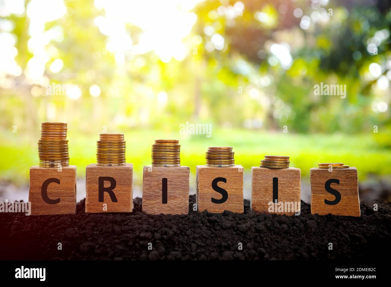 Wirtschafts- und Finanzkrise Rezession und Depression Konzept. Abnehmender Münzstapel auf Holzblöcken bei Sonnenuntergang. Stockfoto