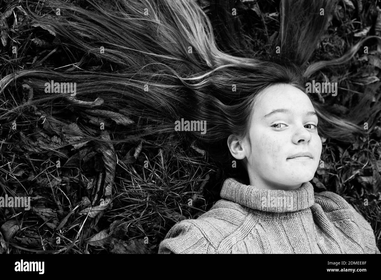 Teen Mädchen liegt auf dem Boden mit langen Haaren auf dem Gras verstreut. Schwarzweiß-Foto. Stockfoto