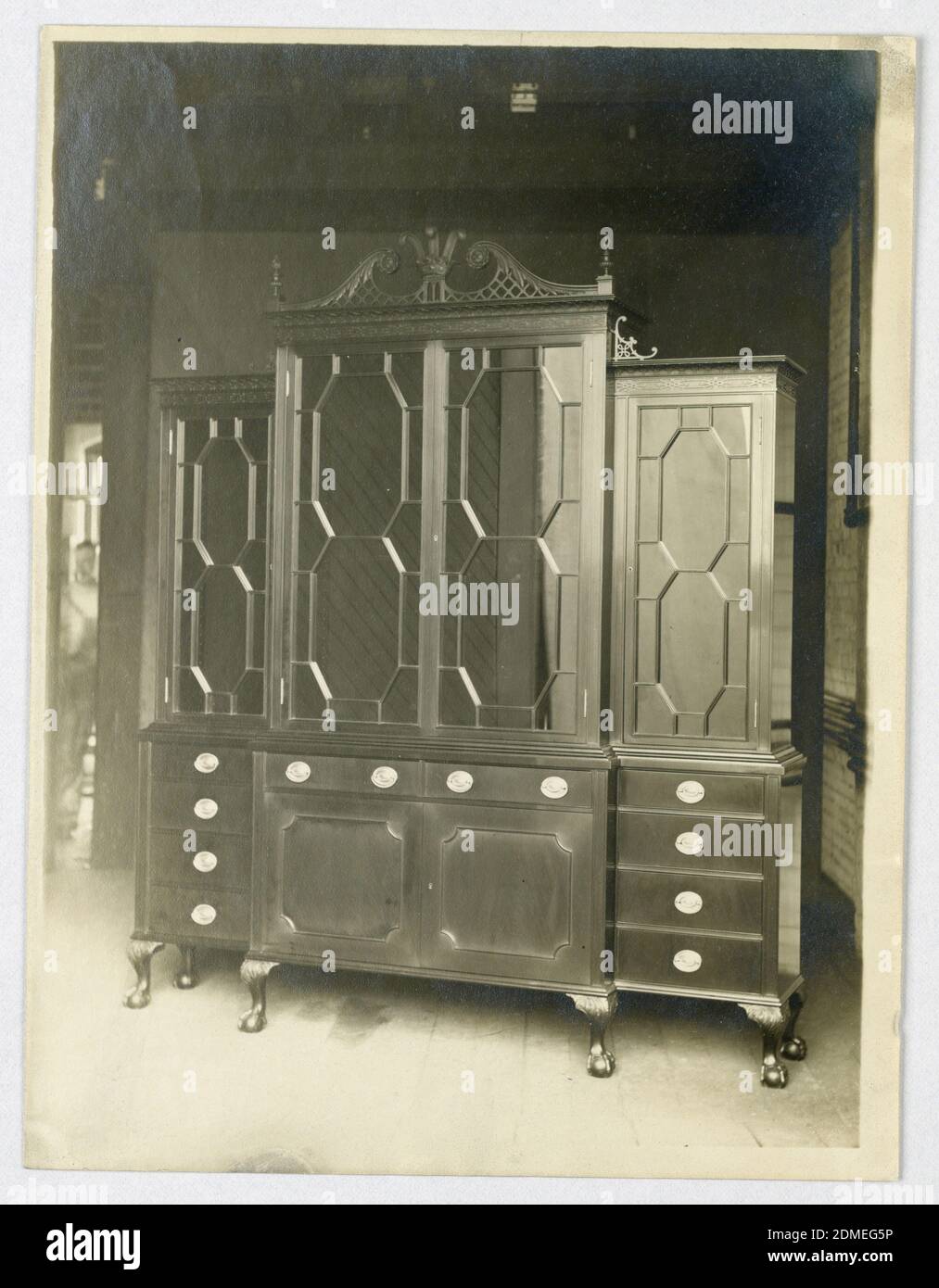 Tall China Kabinett mit gebrochenem Giebel, A. N. Davenport Co., Foto auf Papier, hoher porzellanschrank mit leicht konvexem Mittelsegment bestehend aus 2 Türen und 2 Schubladen, gekrönt von einem großen 2-türigen Abschnitt, der von gebrochenem Giebel, bestehend aus schrotenartigen Elementen mit Laub und Krone mit 3 Federn Mitte und Endstücke auf beiden Seiten, überragt wird; Seitenschränke bestehen aus 4 Schubladen, die von einem großen eintürigen Abschnitt mit geschnitztem chinesischem Laubsägewerk überragt werden; Schrank, der auf 6 kurzen Kabinenbeinen mit geschnitzten Kugelfüßen angehoben wird., 1900–05, Möbel, Foto Stockfoto