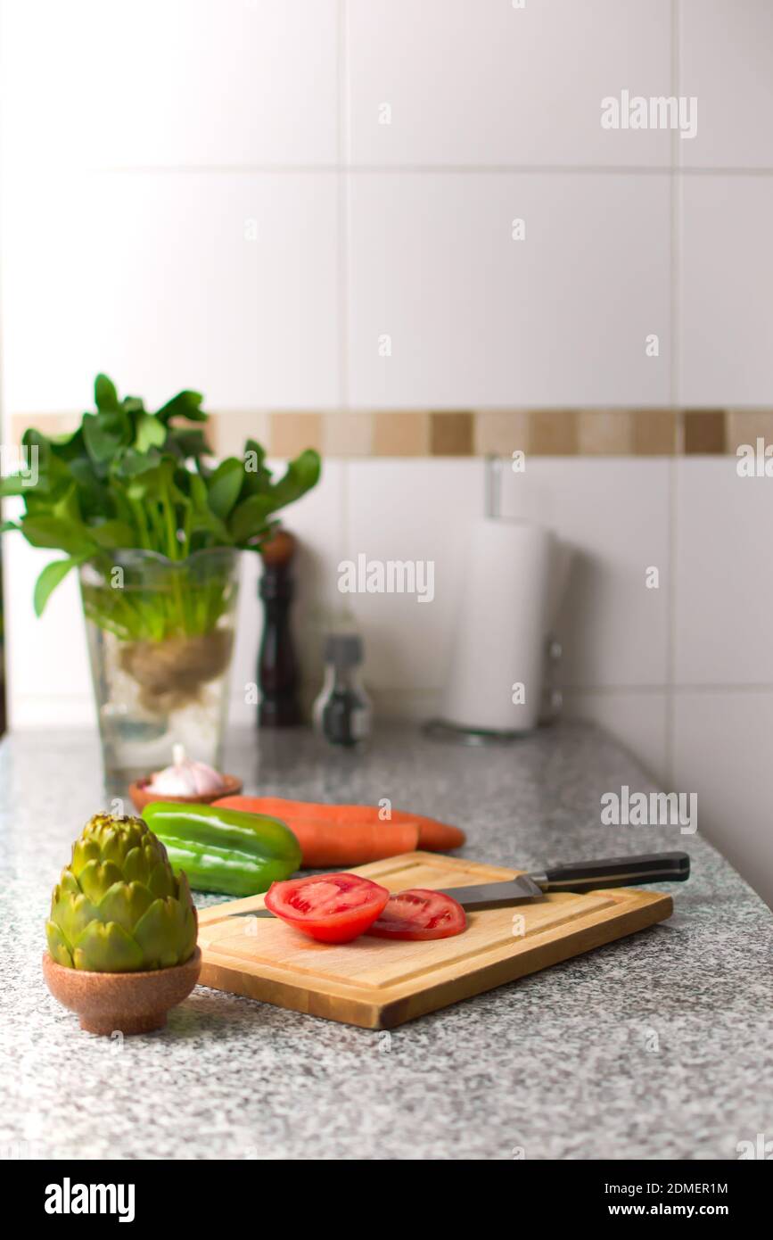 Paprika auf einem Schneidebrett und frische Zutaten über einer Küchenarbeitsplatte. Stockfoto