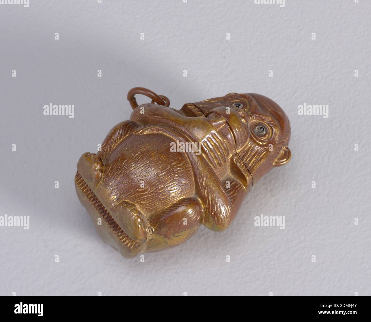 Sitzender Affe, patiniertes Messing, Glas, in Form eines sitzenden Affen, mit gefalteten Armen an der Vorderseite und dem rechten Daumen, der seinen Mund berührt, mit Messingfarben und rötlich-brauner patinierter Oberfläche, Glasaugen. Kopf, der als Deckel dient, auf der Rückseite aufklappbar. Link an seinem oberen rechten Arm befestigt. Stürmer in versenkter Nut unten, unter seinen Füßen. Box kann aufrecht auf dem Tisch sitzen., Ende des 19. Jahrhunderts, Container, Dekorative Kunst, Matchsafe, Matchsafe Stockfoto