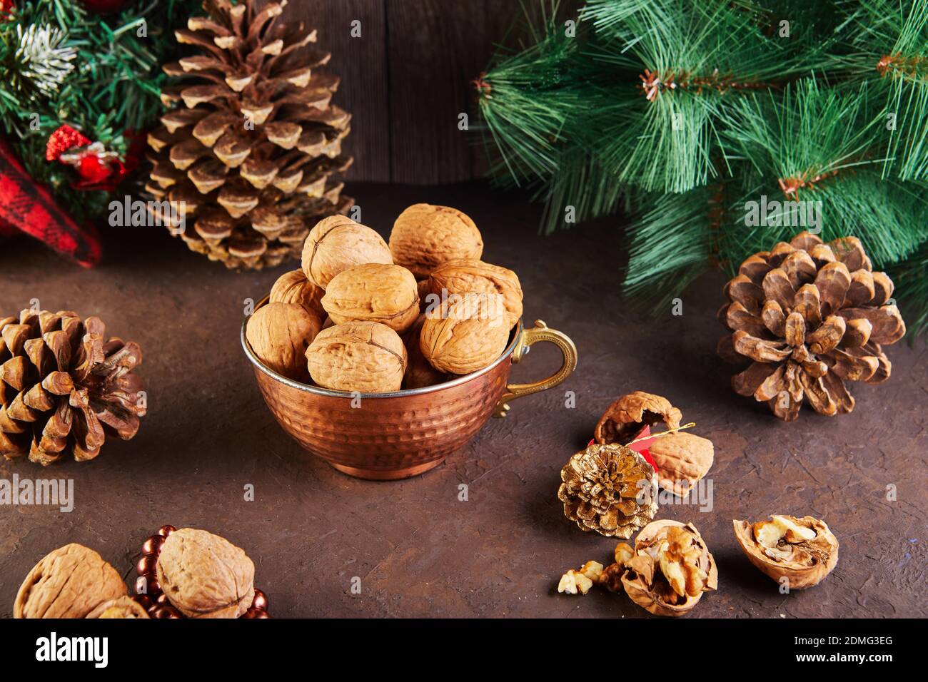 Walnüsse in einem Blechbecher, ganz und gehackt, neben der Füllung und Schalen. Präsentiert in einer Neujahrskomposition mit Tannenzapfen. Home Lagerung des Winters Stockfoto