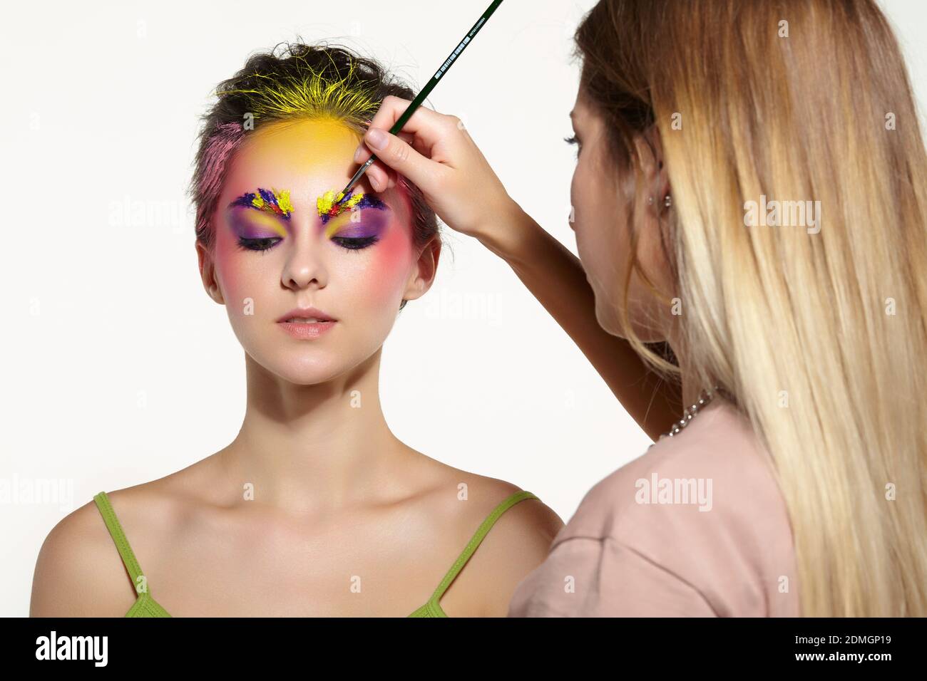 Weibliche Porträt mit ungewöhnlichen Gesicht Kunst Make-up. Farbe auf Augenbrauen, Haare und um die Augen. Künstler Hand mit Pinsel Malerei schöne Mädchen Brauen machen Stockfoto