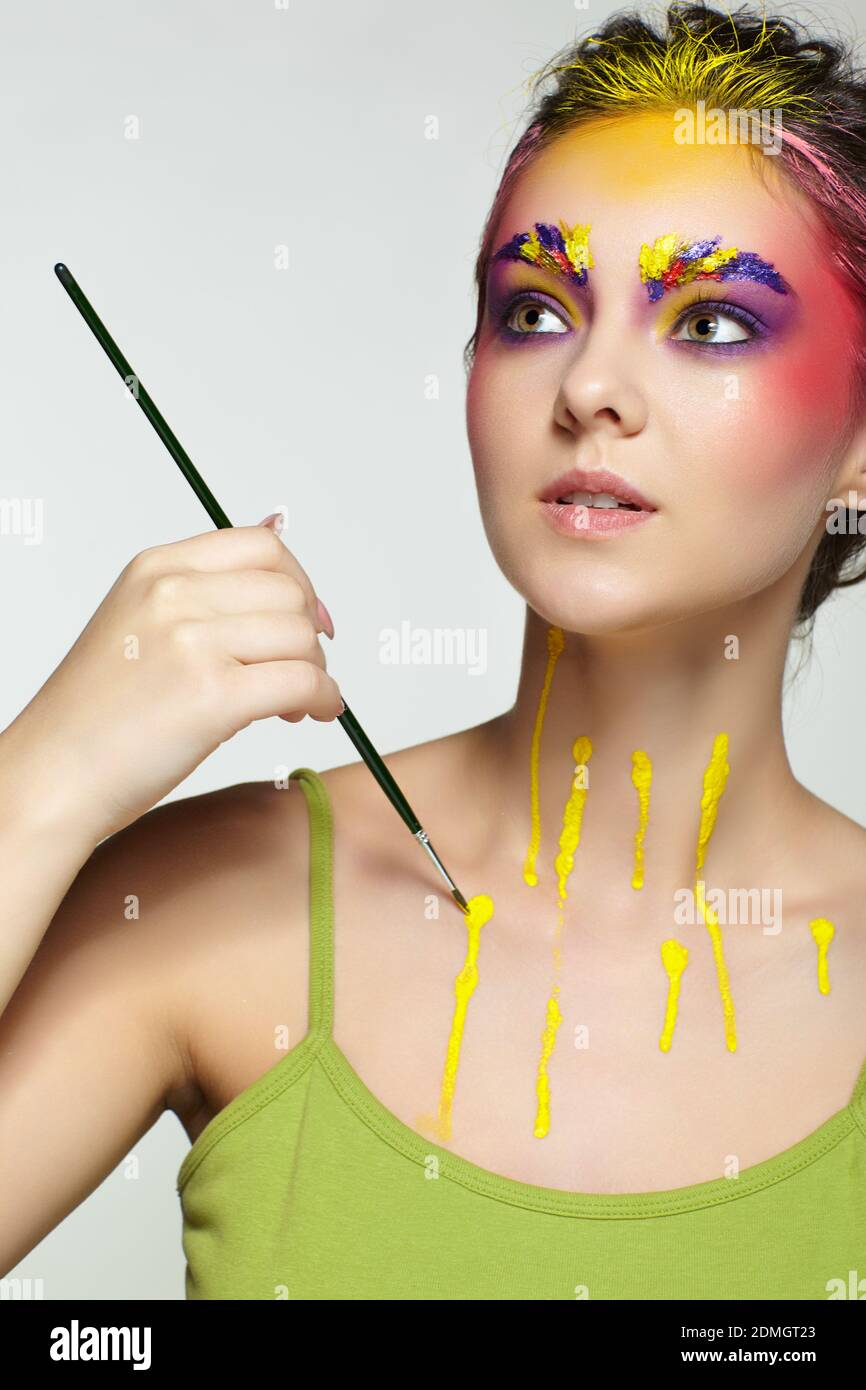 Frauenportrait mit ungewöhnlichem Gesicht und Body Art Make-up. Farbe auf Augenbrauen, Haare, um die Augen und mit Farbe tropft auf den Hals. Frau malt sich mit Stockfoto