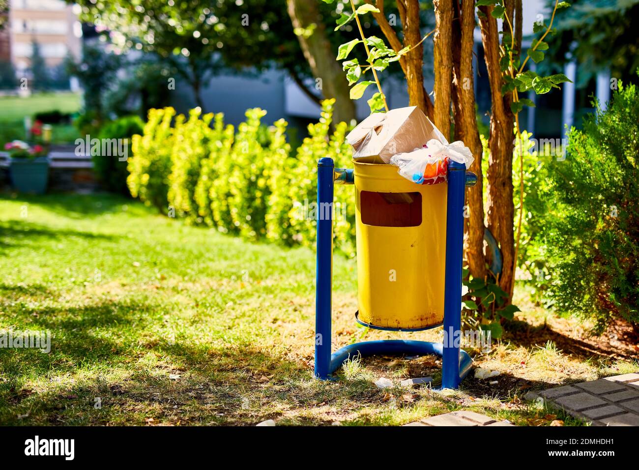 Gelber Metallmüll oder Mülltonne auf dem Gras eines Parks. Müllcontainer im Freien gefüllt mit Müll. Stockfoto