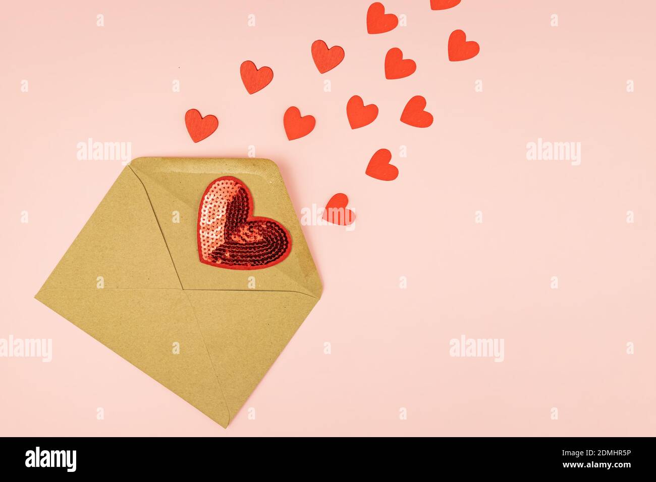 Papierhandwerk Umschlag mit streuenden roten Herzen auf rosa Hintergrund. Mit Kopierbereich. Kreatives Layout für den Valentinstag Stockfoto